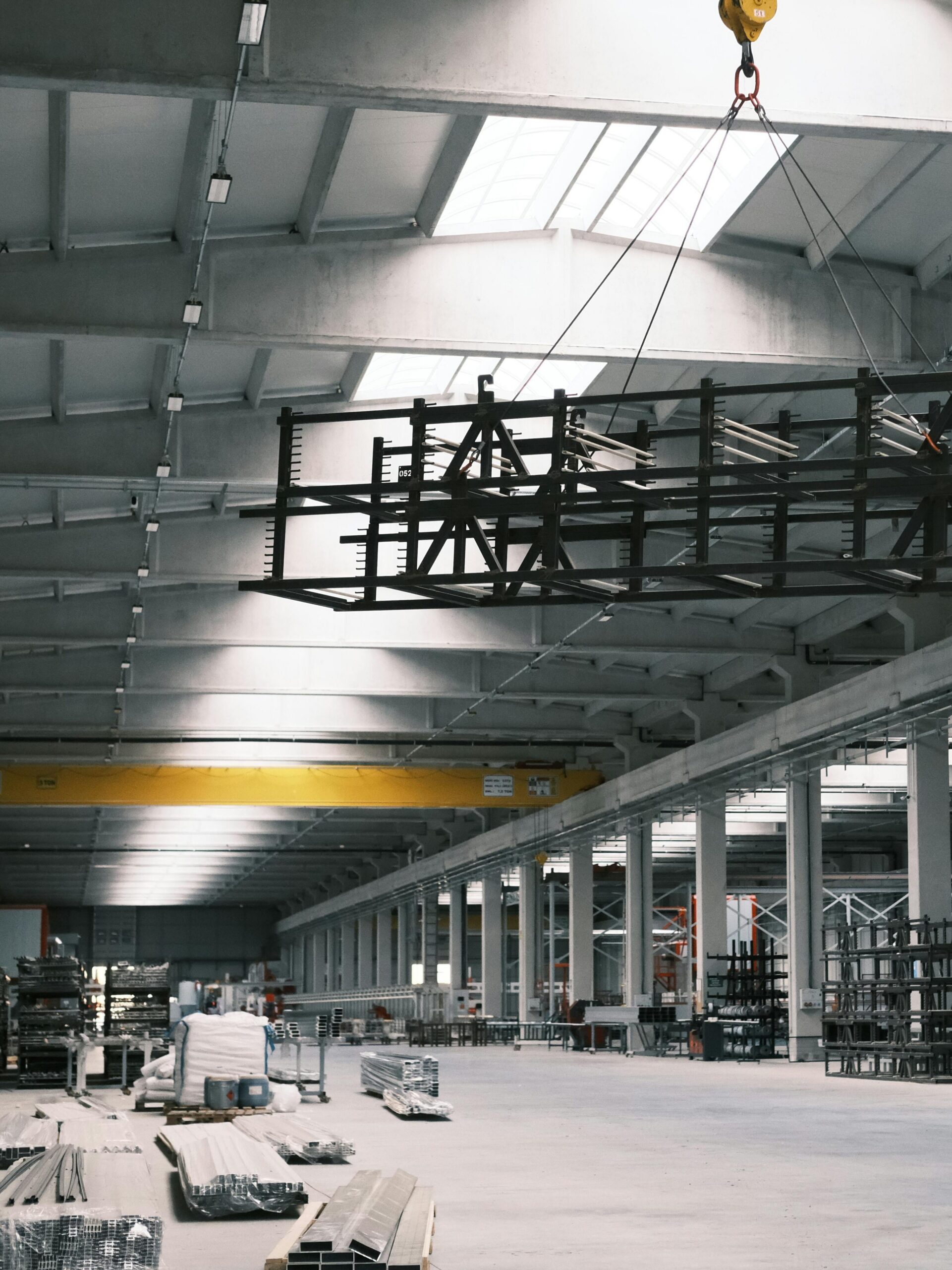 aerospace Spacious industrial warehouse interior with a yellow crane lifting metal framework.