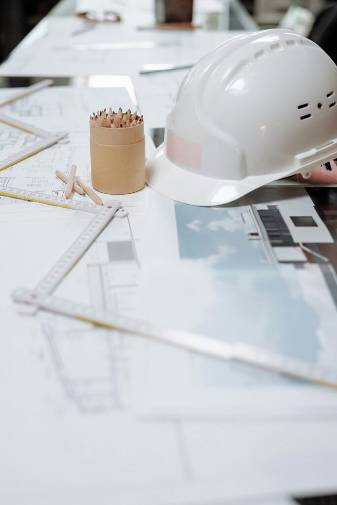 Home A detailed view of an architect's desk with plans, a hard hat, and drafting tools.
